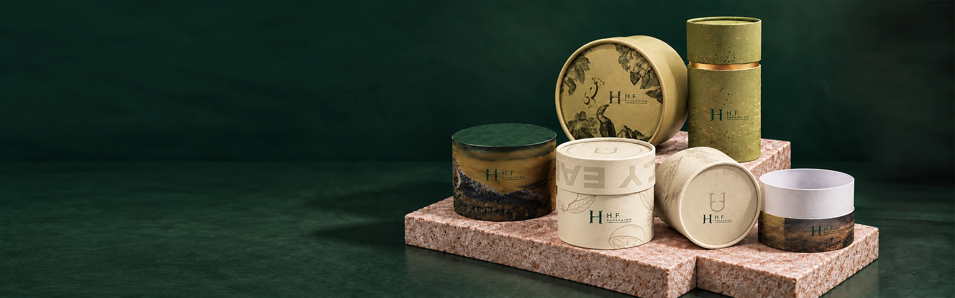 Ivory and sage cosmetic paper tubes with H.F Packaging logos on a deep green studio backdrop