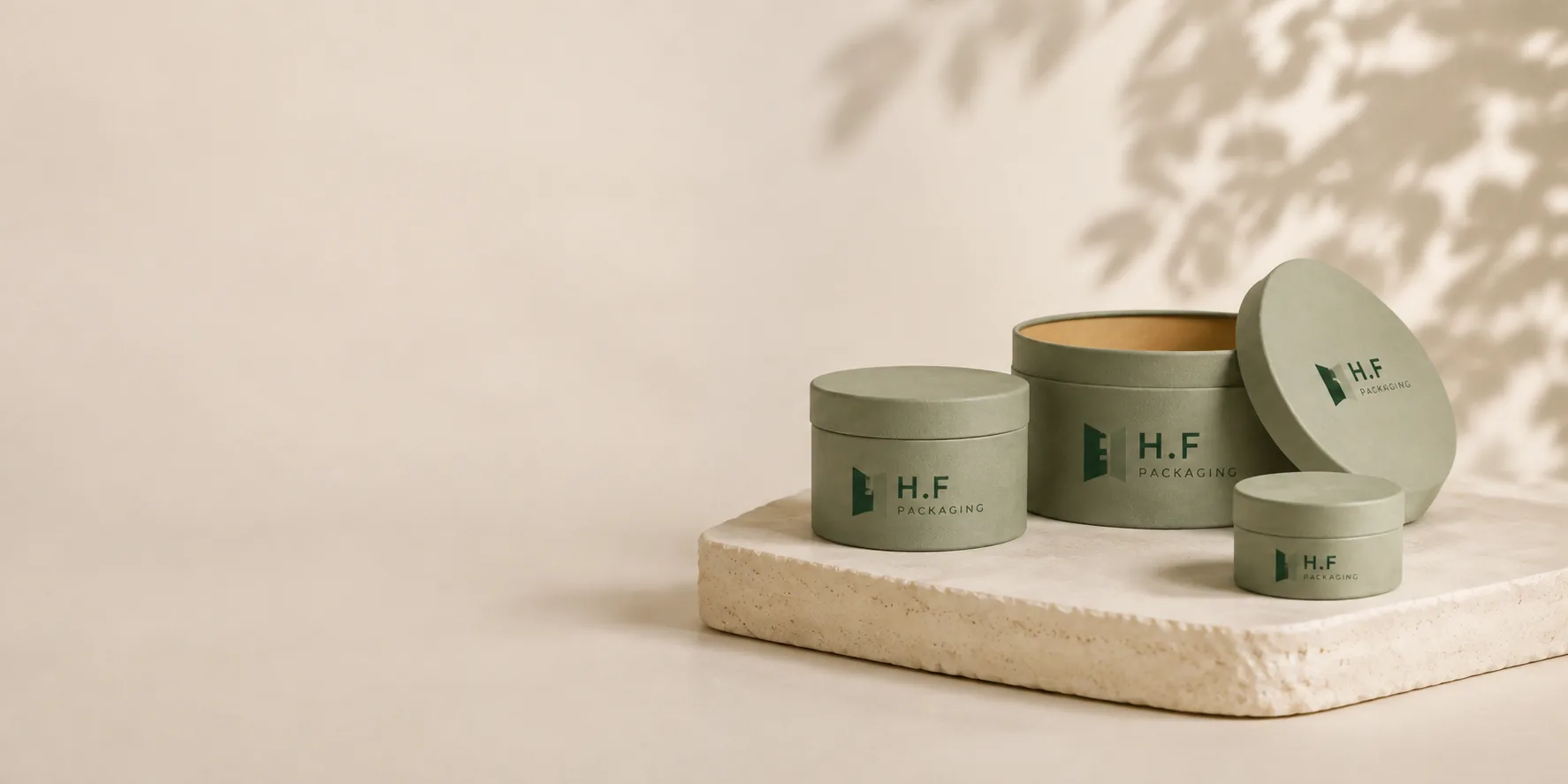 Ivory and sage cosmetic paper tubes with H.F Packaging logos on a deep green studio backdrop